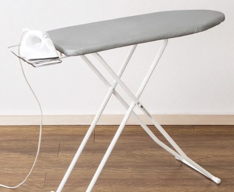 The ironing board with the iron resting on the metal rest at its end